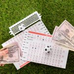 partial view of female hands with dollar banknotes near toy soccer balls, gates and betting lists on